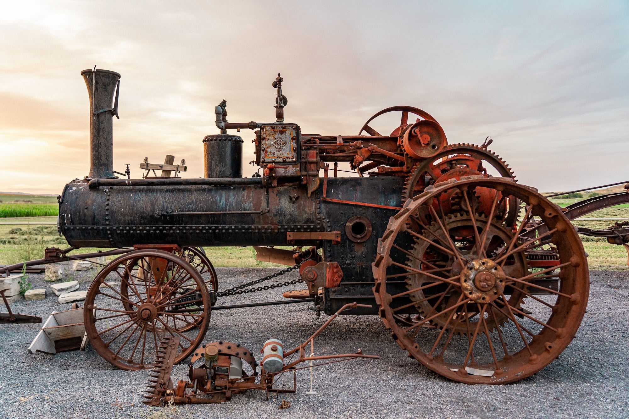 Antique metal steam traction engine with rust and wheels in an open field.